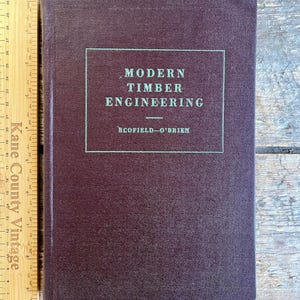 May include: A burgundy hardcover book with the title "MODERN TIMBER ENGINEERING" and the author "BCOFIELD-O'BRIEN" printed in green on the front cover.