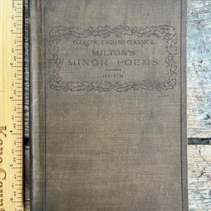 May include: A vintage book titled "Milton's Minor Poems" with the text "Eclectic English Classics" above. The cover is a muted brown color with a decorative border. A wooden ruler is placed next to the book.