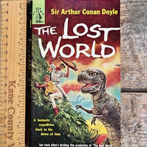 May include: Vintage paperback book cover for "The Lost World" by Sir Arthur Conan Doyle. The cover features a dramatic illustration of a dinosaur and two people in a jungle setting. The book is from the Pyramid series and priced at 35 cents.