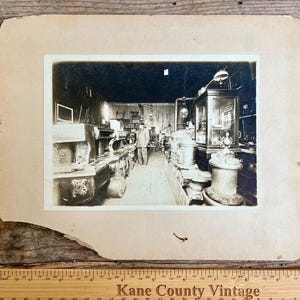Könnte beinhalten: Schwarzweißfoto eines Vintage-Ladengeschäfts mit Regalen voller antiker Gegenstände. Der Laden ist gut beleuchtet und hat eine hohe Decke. Eine Person steht in der Mitte des Ladens und betrachtet die Gegenstände in den Regalen.