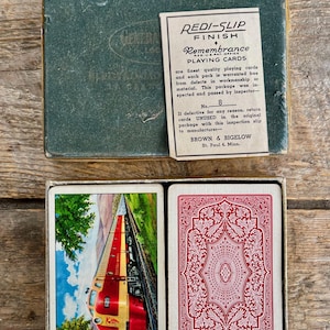 Puede incluir: Baraja de cartas Remembrance vintage en una caja verde. Las cartas presentan una escena de tren y un diseño rojo adornado. La caja incluye una tarjeta Redi-Slip Finish de Brown & Bigelow, St. Paul 4, Minn.