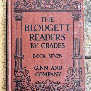 May include: A red hardcover book with a black ornate border and the title "The Blodgett Readers by Grades Book Seven Ginn and Company".