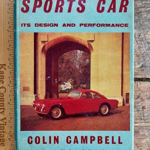 Puede incluir: Libro antiguo titulado "The Sports Car" con un coche deportivo rojo en la portada. La portada es azul claro con texto rojo y blanco. El autor es Colin Campbell.