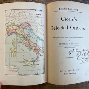Puede incluir: Libro abierto con un mapa de Italia en la página izquierda y texto en la derecha. El mapa en color muestra regiones y ciudades. La página derecha presenta el título "Cicero's Selected Orations."