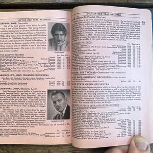 Puede incluir: Libro abierto con páginas rosas con texto y retratos en blanco y negro. El libro se titula "Victor Red Seal Records" e incluye información sobre músicos y orquestas. El libro está abierto sobre una superficie de madera.