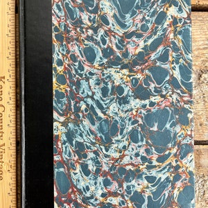 May include: A dark blue book with a marbled cover featuring swirls of red, white, and gold. The book has a black spine.