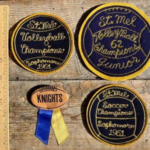 May include: Four embroidered patches with gold stitching on a blue background. The patches are for volleyball, football, soccer, and a general sports patch with the word "Knights". The patches are all from St. Mel's and are from 1961.
