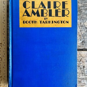 May include: A blue hardback book with a yellow label that reads "CLAIRE AMBLER BY BOOTH TARKINGTON".