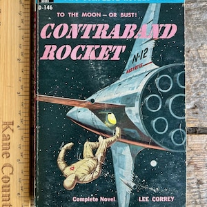May include: Vintage paperback book cover titled "Contraband Rocket" with a space theme. The cover features a rocket ship, a spaceman, and the text "To the Moon - Or Bust!" in pink and white. The book is by Lee Correy.