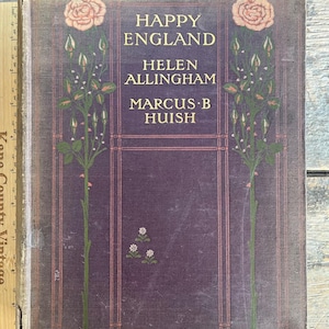 Puede incluir: Un libro antiguo titulado "Happy England" de Helen Allingham y Marcus B. Huish. La portada es de color púrpura oscuro con letras doradas y elementos florales decorativos. Dos rosas rosas y tallos verdes estilizados con capullos flanquean el título.