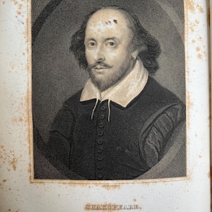 Op de afbeelding: Een zwart-wit portret van William Shakespeare, een beroemde Engelse toneelschrijver en dichter. De afbeelding is afkomstig uit een boek en bevat de tekst "SHAKSPEARE." en "From the Picture in the Possession of the Duke of Buckingham it here."