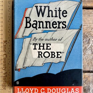 May include: A vintage book cover with a blue background and white banners. The title "White Banners" is in black text. The book is by Lloyd C. Douglas, author of "The Robe".