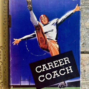 Puede incluir: Una portada de libro vintage con fondo azul que muestra a un jugador de fútbol americano pateando una pelota. El título del libro es "CAREER COACH" de EARL SCHENCK MIERS.
