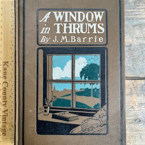 Puede incluir: Un libro antiguo titulado "A Window in Thrums" de J.M. Barrie. La portada marrón presenta una ilustración enmarcada de una ventana con vistas a un paisaje. El título es blanco y el libro parece estar en buen estado.