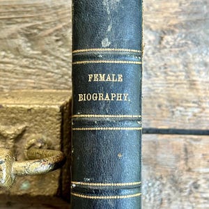 May include: A black leather-bound book with gold lettering. The title is "FEMALE BIOGRAPHY" and the author is "KNAPP".
