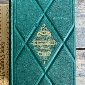 May include: A vintage hardcover book titled "Religious Denominations of the World." The book has a textured, dark green cover with a diamond pattern. Gold lettering and embellishments are featured on the cover.