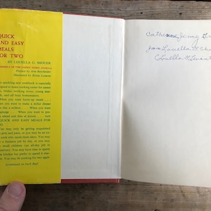 May include: A yellow and green cookbook titled "Quick and Easy Meals for Two" by Louella G. Shouer. The book is open to the first page, which includes a preface by Ann Batchelder and illustrations by Reisie Lonette. The book is designed to make cooking easier for busy people.