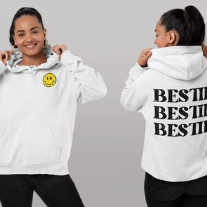 May include: White hoodie with a yellow smiley face on the front and the word "BESTIE" repeated three times on the back.