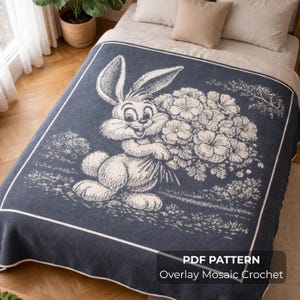 May include: A navy blue blanket with a white border and a large illustration of a smiling rabbit holding a bouquet of flowers. The blanket has a textured appearance and is displayed on a bed.