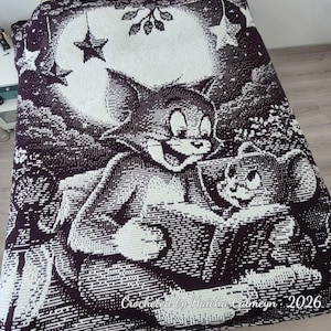 May include: A dark purple and white crocheted blanket featuring a large graphic of Tom and Jerry in front of a full moon with stars. The bottom right corner includes the text Crocheted by Haicha Calmeyn 2026 in a white cursive script font.