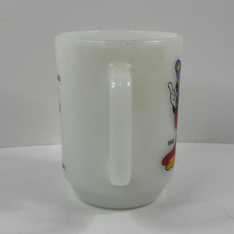 May include: White ceramic mug featuring a colorful Mickey Mouse graphic. The mug has a curved handle and the year "1940" is printed on the side. The mug is a vintage collectible.
