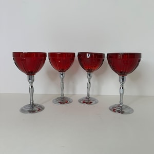May include: Four ruby red stemmed glasses with a decorative pattern on the bowl. The stems and bases are silver-toned. The glasses are arranged in a row against a white background. These vintage glasses are perfect for serving cocktails.