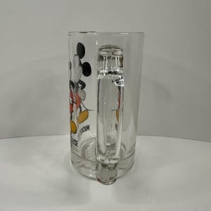 Peut inclure: Une chope &agrave; bi&egrave;re en verre transparent orn&eacute;e d'un motif de Mickey Mouse portant un short rouge et des chaussures jaunes. Le c&ocirc;t&eacute; de la chope affiche le texte Mickey Mouse en lettres noires. Elle poss&egrave;de une anse solide et une base &eacute;paisse.