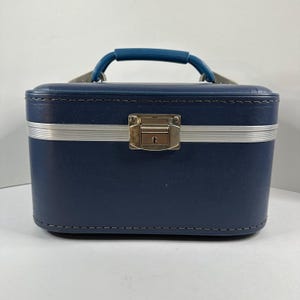 May include: A vintage navy blue vanity case with a silver band and a teal handle. The rectangular case has a metal clasp closure. The handle is curved and attached to the top of the case with silver hardware.