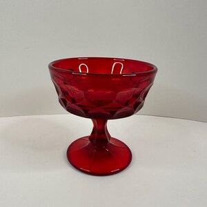 May include: A ruby red glass dessert dish with a textured, diamond-patterned bowl and a stemmed base. The dish is designed for serving desserts and is approximately 4 inches tall.
