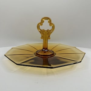 Puede incluir: Bandeja de servir de dos niveles de color ámbar con asa decorativa. La bandeja tiene forma octogonal con un diseño radiante. El asa es ornamentada. Ideal para servir aperitivos o postres. Una pieza vintage.