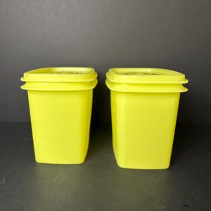 May include: Two matching, square, yellow plastic containers with lids. The containers are a bright, solid yellow colour and have a slightly textured appearance. The lids fit snugly on top, creating a tight seal. The containers are likely for food storage.