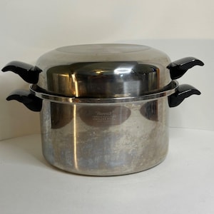 May include: Stainless steel steamer pot with black handles. The pot has a shiny, reflective surface and a lid. The pot is designed for steaming food and has a classic, functional design.