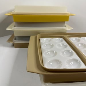 Puede incluir: Un juego de recipientes de plástico beige con un inserto de bandeja para huevos blanco. Los recipientes están apilados uno encima del otro. La bandeja para huevos tiene 12 compartimentos individuales para huevos.