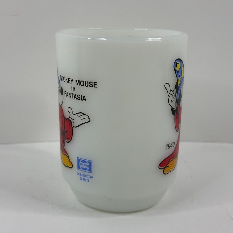 May include: White glass tumbler featuring Mickey Mouse from Fantasia. The tumbler has a design of Mickey Mouse in a red robe and blue hat. The text "Mickey Mouse in Fantasia" and "1940" are printed on the tumbler. The Pepsi Collector Series logo is also visible.