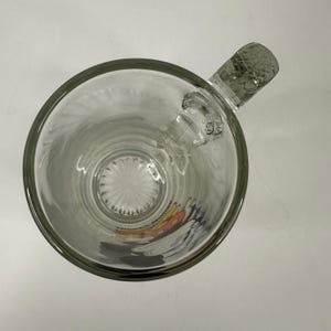 Peut inclure: Une tasse en verre transparent vue du dessus, dot&eacute;e d'une anse textur&eacute;e et d'un motif en &eacute;toile sur la base. Un graphique color&eacute; repr&eacute;sentant un personnage de dessin anim&eacute; avec des &eacute;l&eacute;ments noirs, blancs et rouges est visible &agrave; travers.
