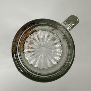 Peut inclure: Une chope &agrave; bi&egrave;re en verre transparent vue directement du dessus, dot&eacute;e d'une anse &eacute;paisse et robuste et d'un motif en &eacute;toile en relief au centre de la base. Le bord circulaire est lisse et le verre pr&eacute;sente une l&eacute;g&egrave;re teinte grise.