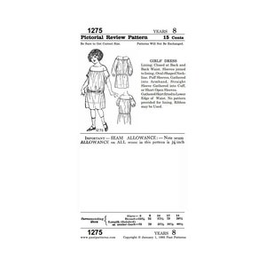 Op de afbeelding: Een zwart-witte lijntekening van een patroon voor een meisjesjurk van Pictorial Review Pattern, nummer 1275. Het patroon is voor maten 6 tot 14 jaar en kost 15 cent. De jurk heeft een geplooide rok, pofmouwen en een ronde halslijn. Het patroon bevat instructies voor het maken van de jurk met of zonder voering.