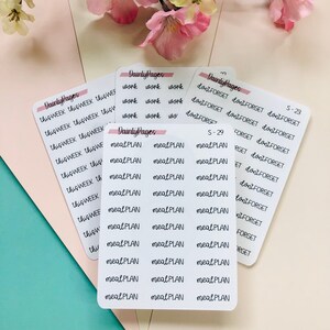 May include: A set of white planner stickers with black handwritten text. The stickers include the phrases "this week", "meal plan", "work", and "don't forget".