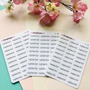 May include: Three sheets of white paper with the text "Dainty Pages" and "S-00" printed on them. Each sheet has multiple rows of the text "Custom Text" repeated.