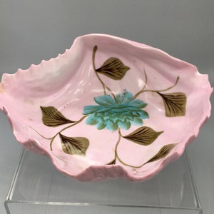 May include: A pink ceramic bowl shaped like a seashell with a painted floral design. The flower is blue and green with brown leaves.