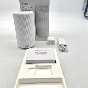 May include: White Smart Fragrance Diffuser with a matching box and accessories. The diffuser has a cylindrical shape with vertical ridges. The box reads "Smart Fragrance Diffuser" and the text "Fill your home with fragrance" is visible on a card.