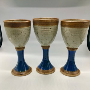 May include: Set of three ceramic goblets with brown, white, and blue glaze. The goblets have a wide bowl and a tall, slender stem.