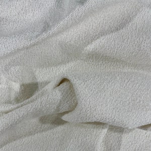 May include: Close-up of a white, textured fabric with a soft, fuzzy appearance. The fabric is folded and draped, showcasing its texture and drape.