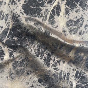 May include: Close-up of a fabric with a textured, abstract pattern in shades of grey and gold.