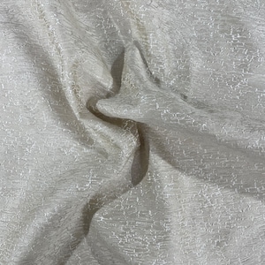 Pode incluir: Close-up de um tecido branco texturizado com um brilho sutil. O tecido está drapeado e dobrado, criando dobras e sombras suaves.