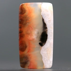 May include: A rectangular gemstone with rounded edges. The stone features a blend of colors, including orange, brown, black, and white. The pattern resembles a landscape with swirling and layered textures. The gemstone is polished and smooth.