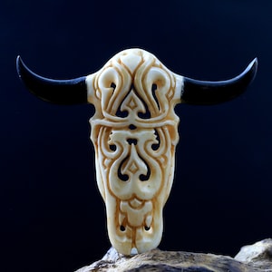 May include: A white carved bull skull with intricate designs and black horns. The skull is a decorative piece with a traditional design.