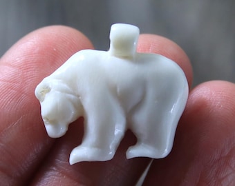 May include: A white carved polar bear pendant. The bear is standing on all fours and has a small loop on its back for hanging.