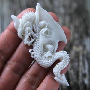 May include: A white dragon carved from bone with intricate details. The dragon is curled up with its wings spread out.