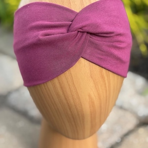 May include: A deep magenta-colored headband with a twisted knot design. The headband is displayed on a wooden head form. The word "Wildberry" is written in cursive script at the bottom of the image.